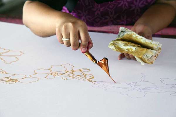 An artist carefully traces the floral motif on a traditional batik fabric using melted wax